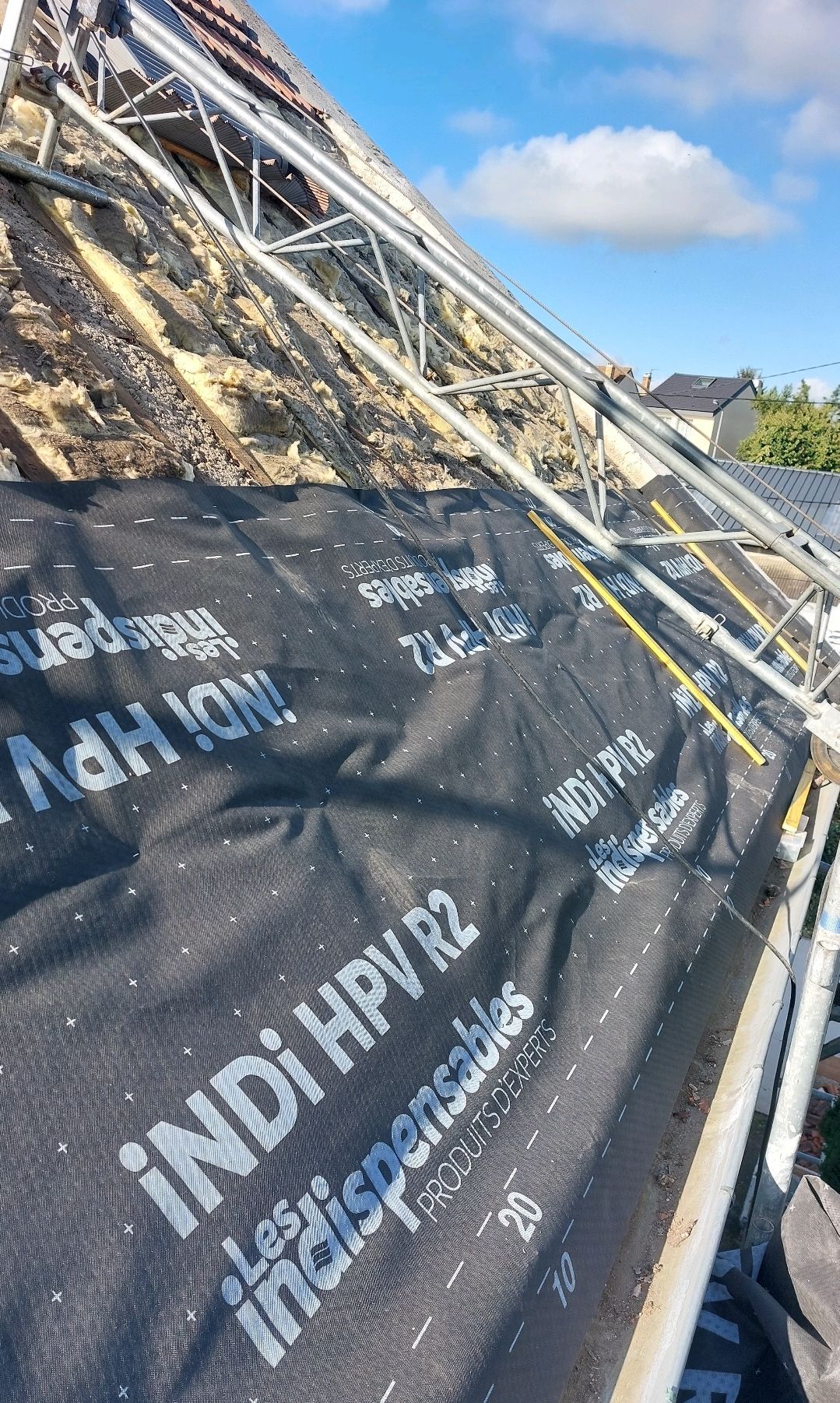 Pose d'une sous-couche de toiture noire sur un toit à l'aide d'échafaudages.