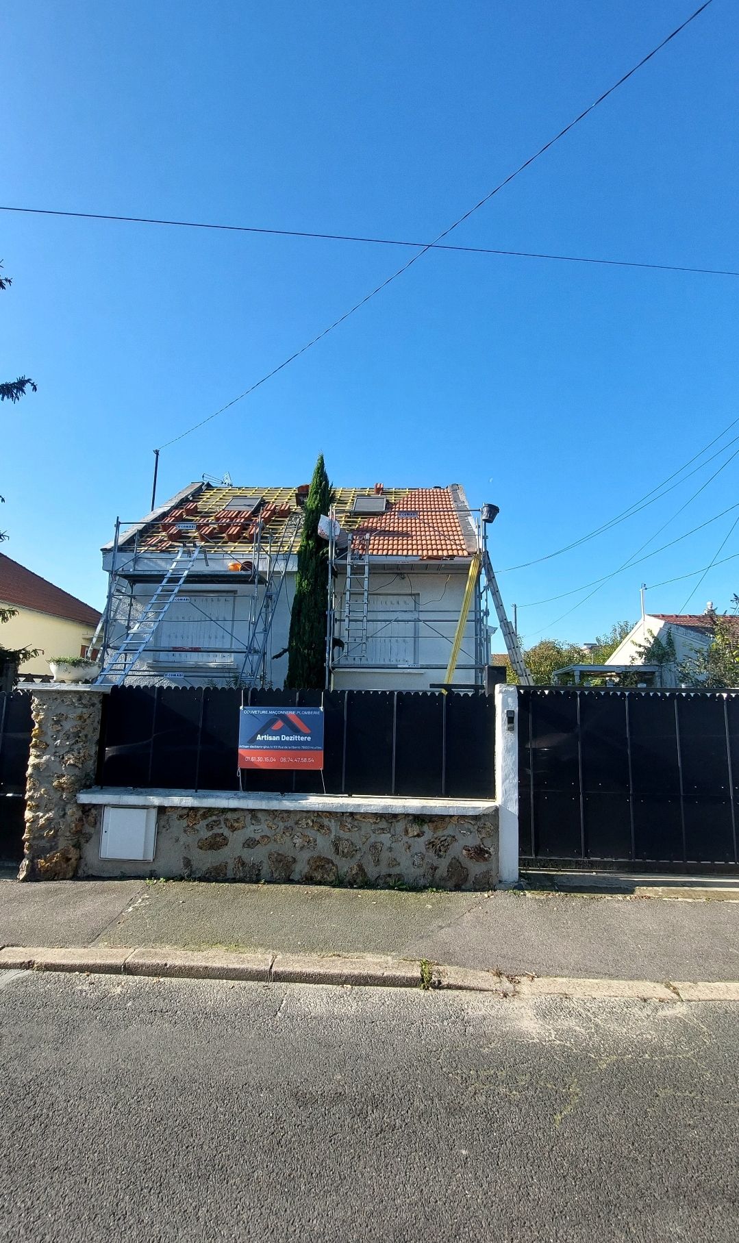 Maison en cours de réparation de toiture, échafaudages et échelle visibles. Ciel bleu.