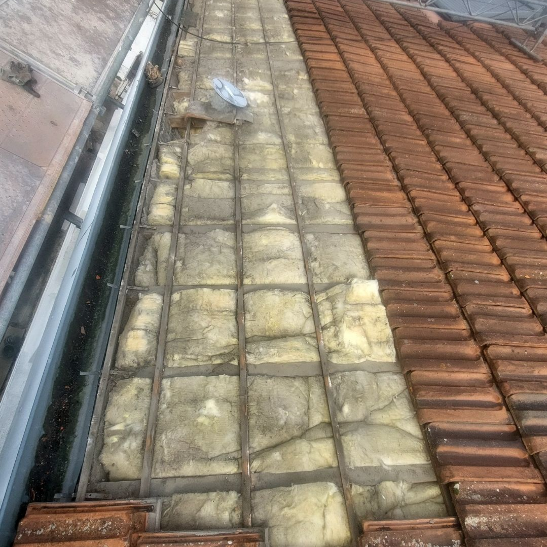 Coupe de toiture montrant l'isolation entre les tuiles et la gouttière.