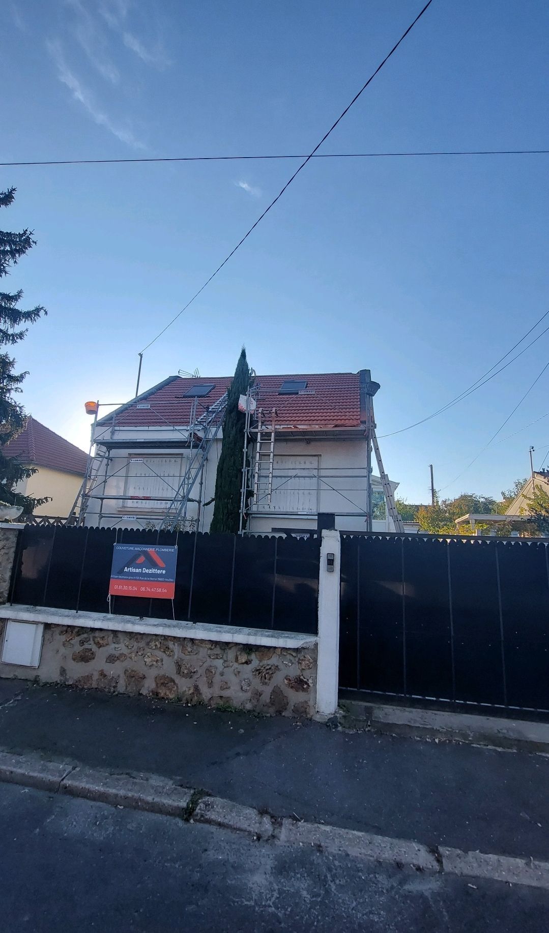 Maison avec des échafaudages pour des travaux de toiture, derrière une clôture noire.