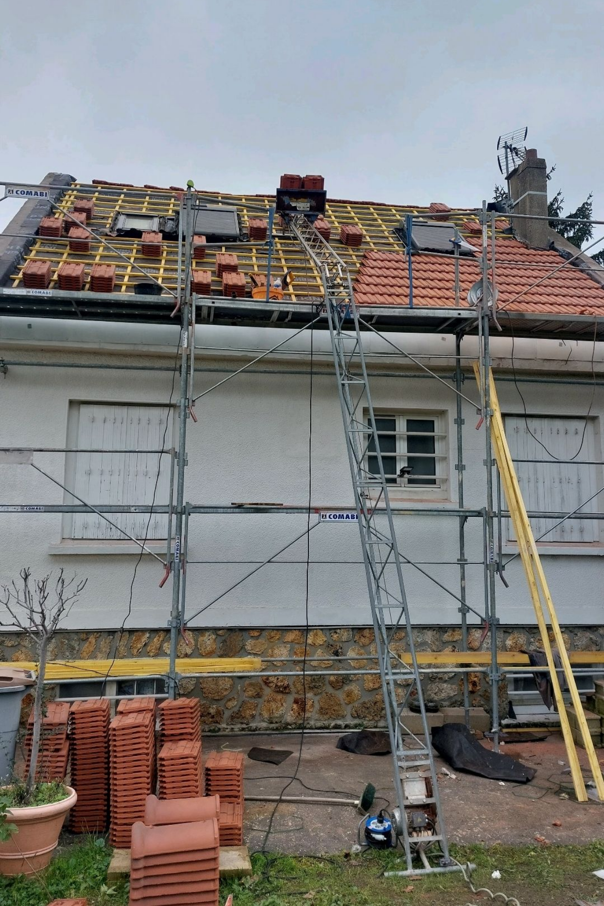 Toiture d'une maison en construction ; échafaudages, tuiles et échelle sont installés.