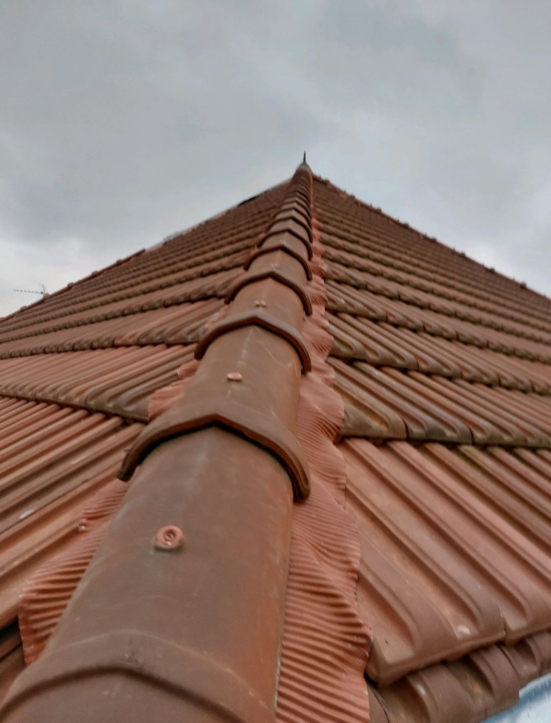 Toit de tuiles en terre cuite rouge, gros plan, sur fond de ciel nuageux.