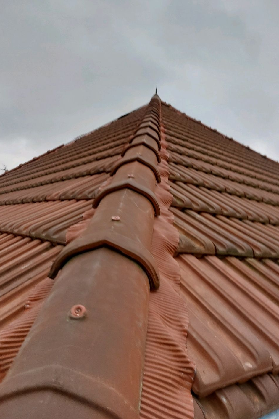 Toit de tuile rouge pointu se détachant sur un ciel nuageux.