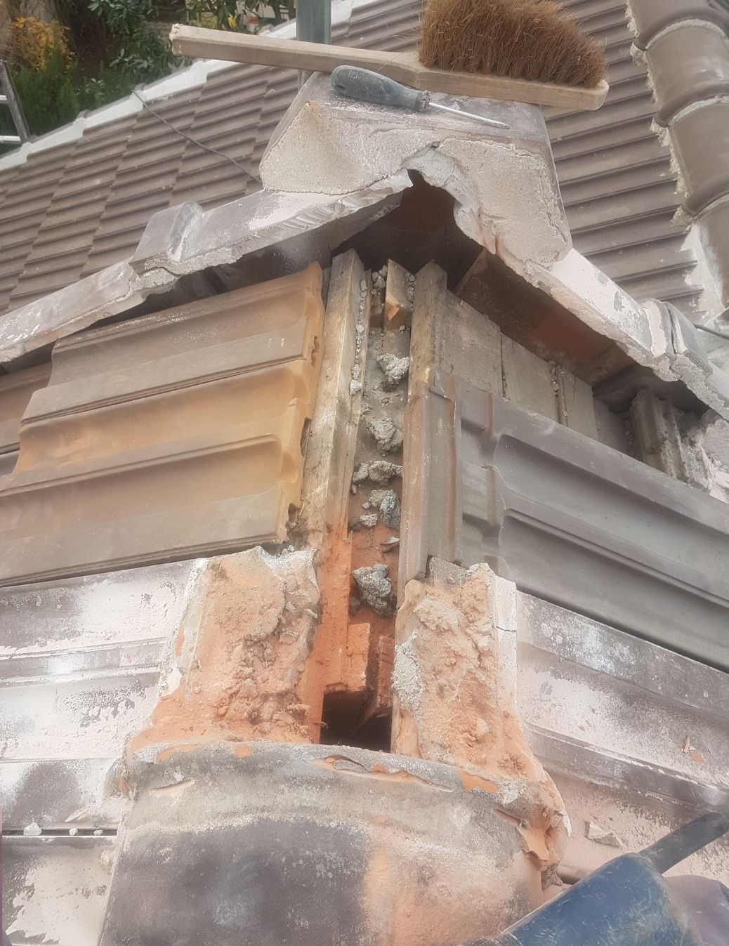 Angle de cheminée endommagé sur un toit, laissant apparaître la charpente et la brique.