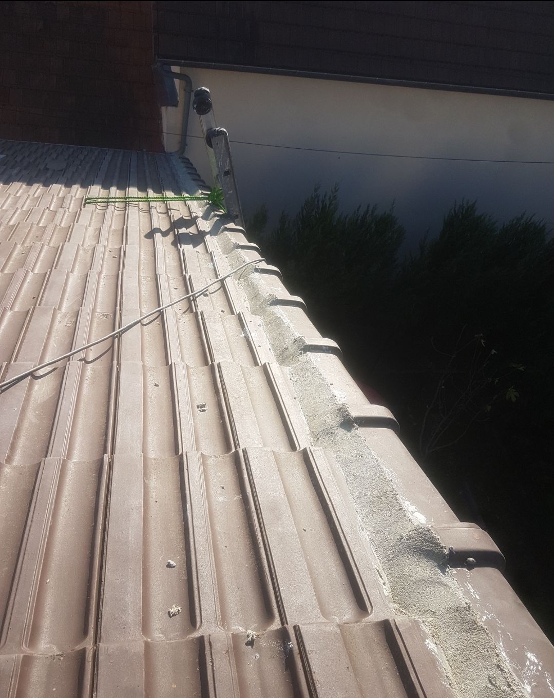 Toit brun avec des débris près du bord, un outil de nettoyage vert repose sur le toit.