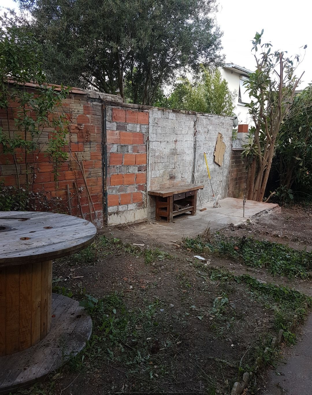 Des murs de brique et de béton entourent un petit banc en bois dans une cour.