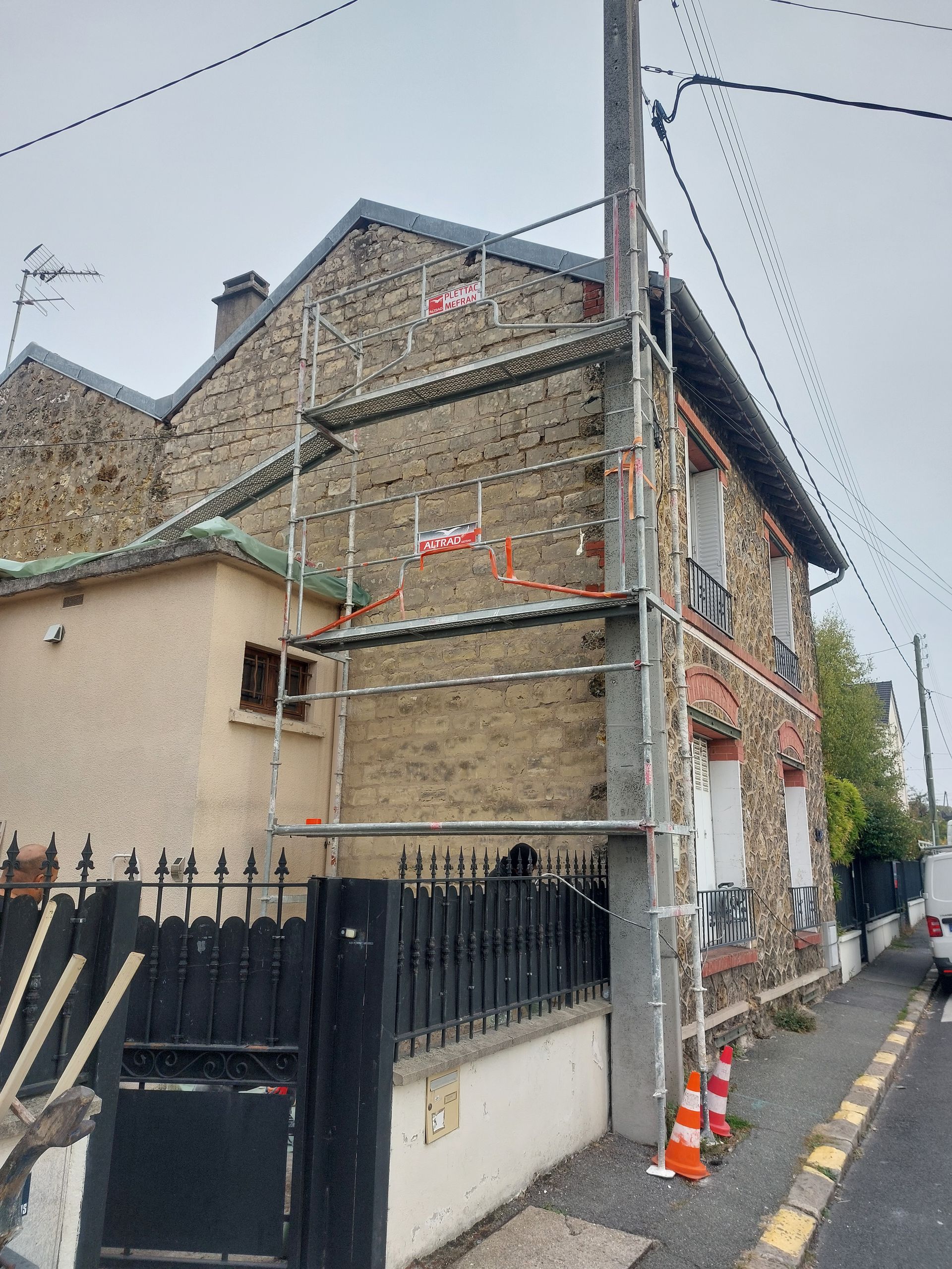 Échafaudages sur le côté d'un bâtiment en pierre. Des cônes orange bordent le trottoir.