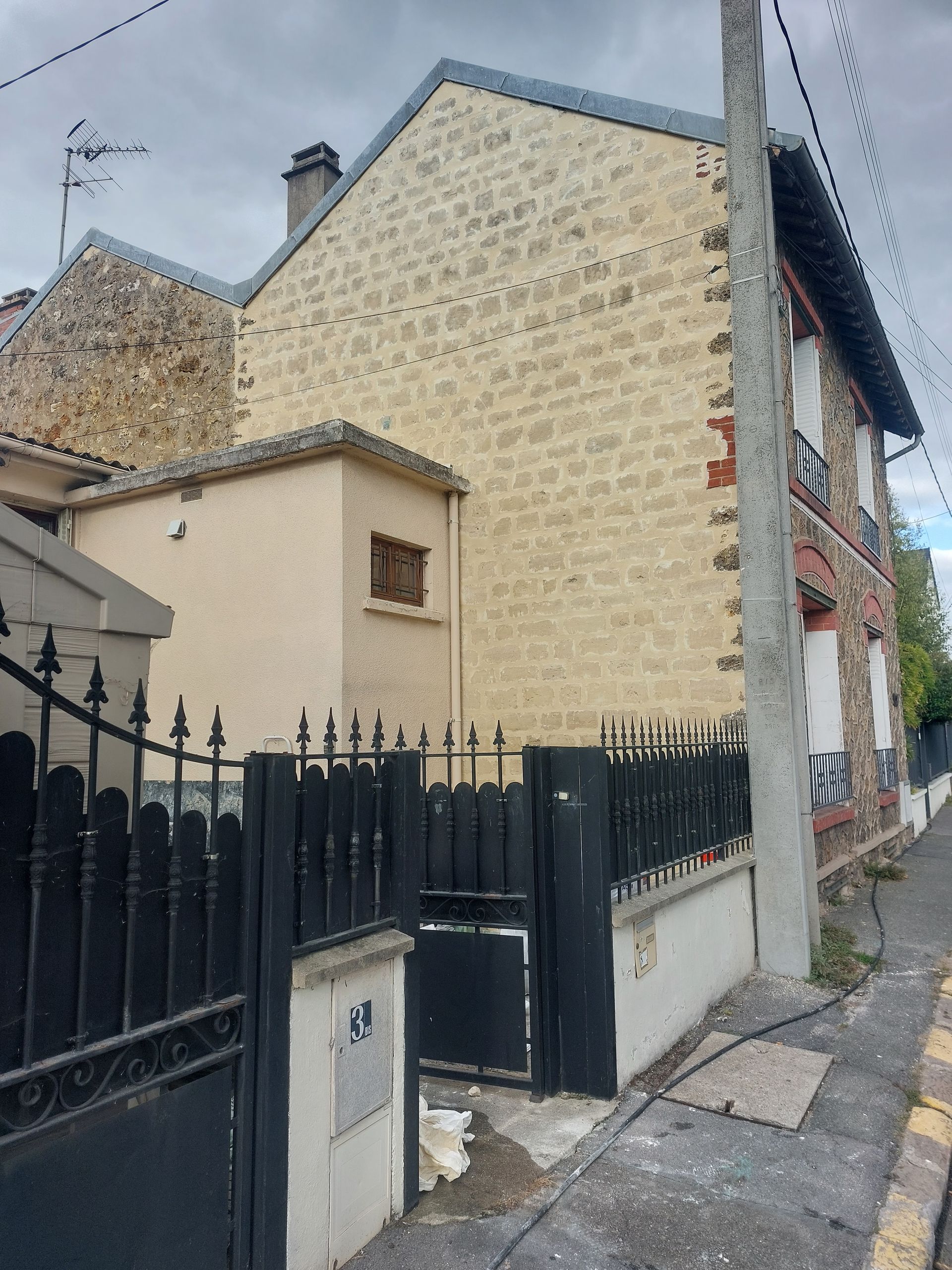 Maison en pierre et en brique avec portail noir et poteau électrique.