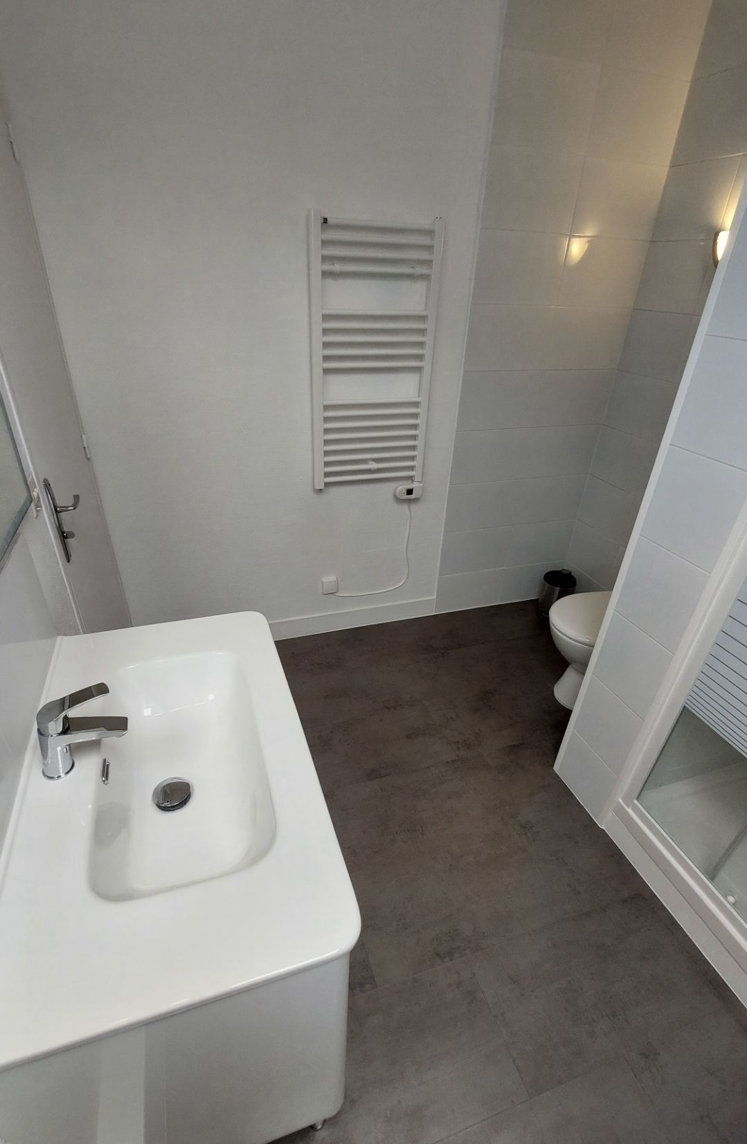 Salle de bains avec lavabo blanc, sol gris, porte-serviettes et toilettes.