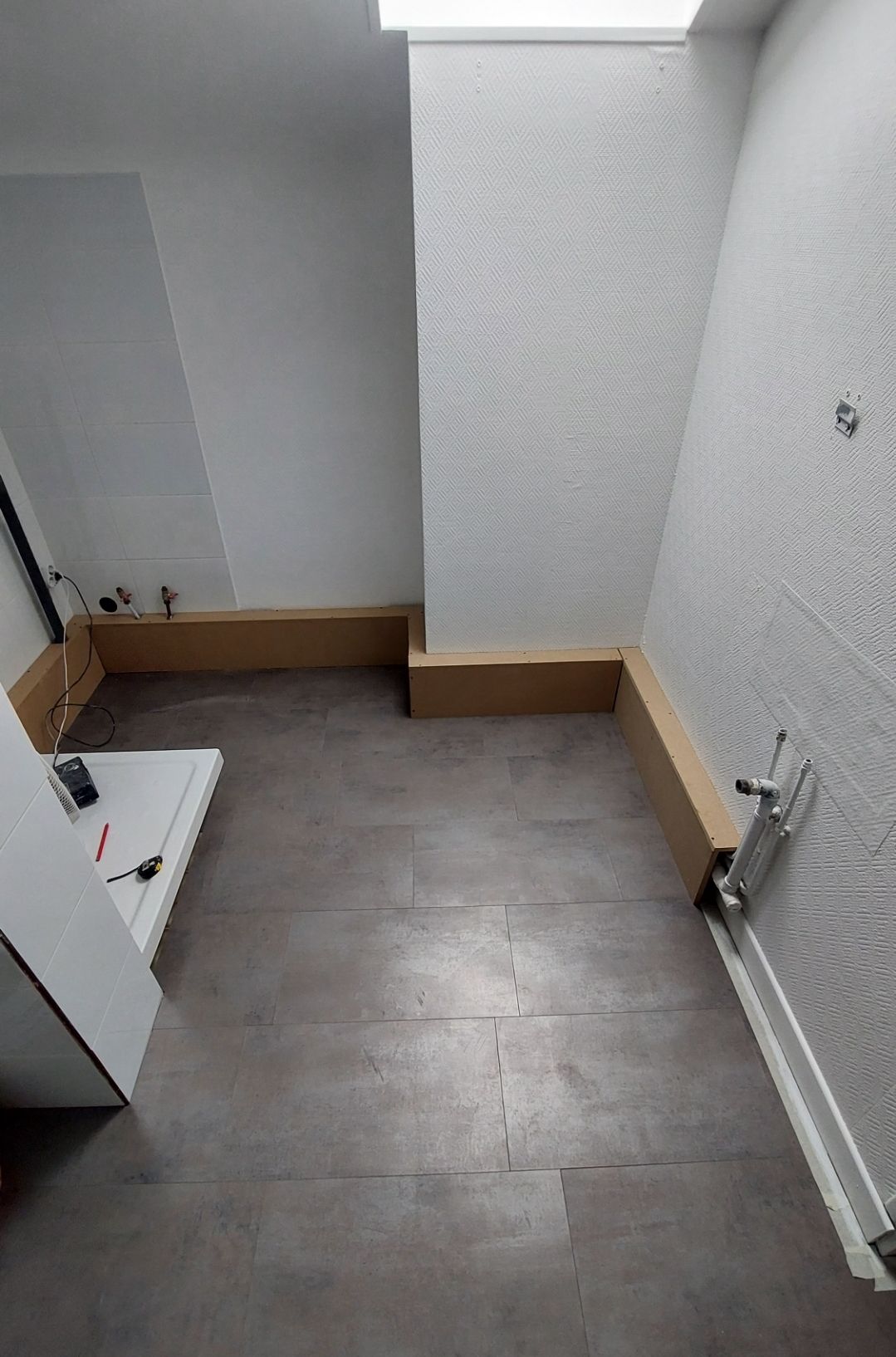 Pièce avec sol foncé, murs blancs texturés, cloison en carton et armoire partiellement ouverte.