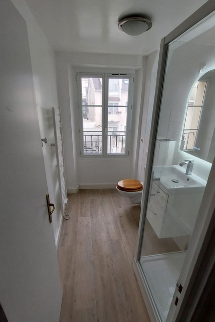 Salle de bains avec douche, lavabo, fenêtre et radiateur, avec parquet clair.