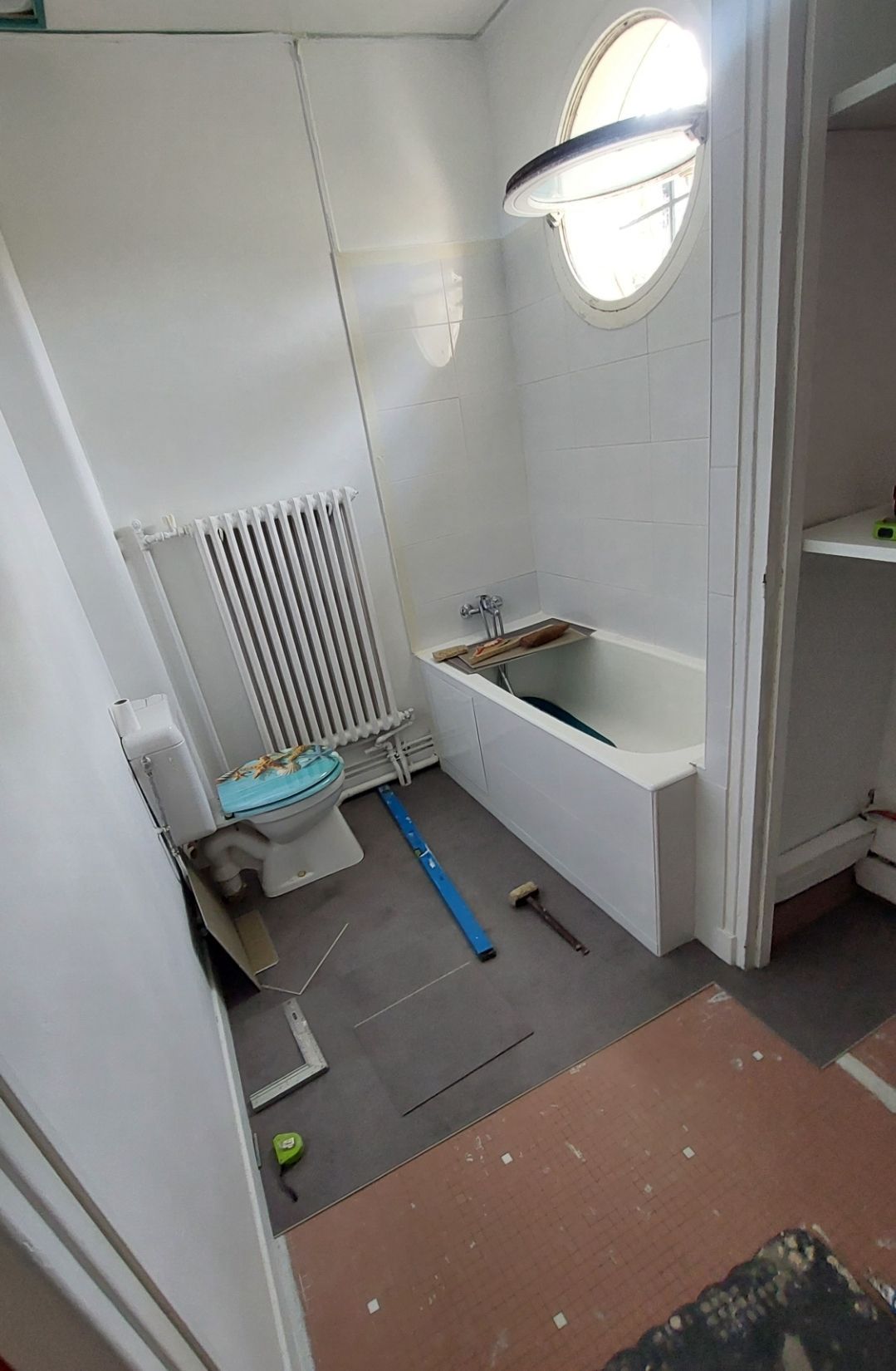 Salle de bains en construction avec baignoire, toilettes, radiateur et nouveau revêtement de sol partiellement installés.