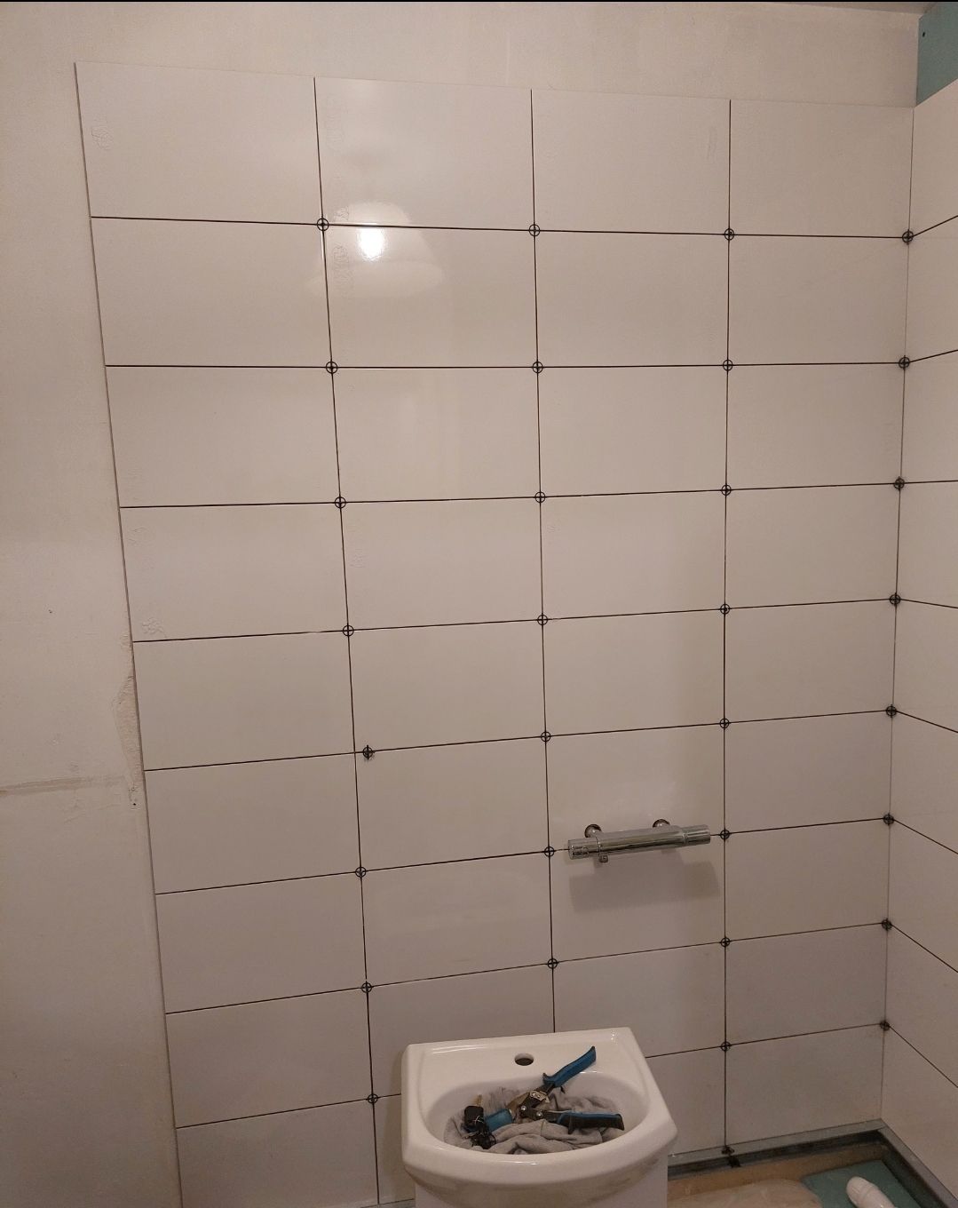 Mur de salle de bains carrelé de blanc avec un accessoire fixé au-dessus des toilettes.