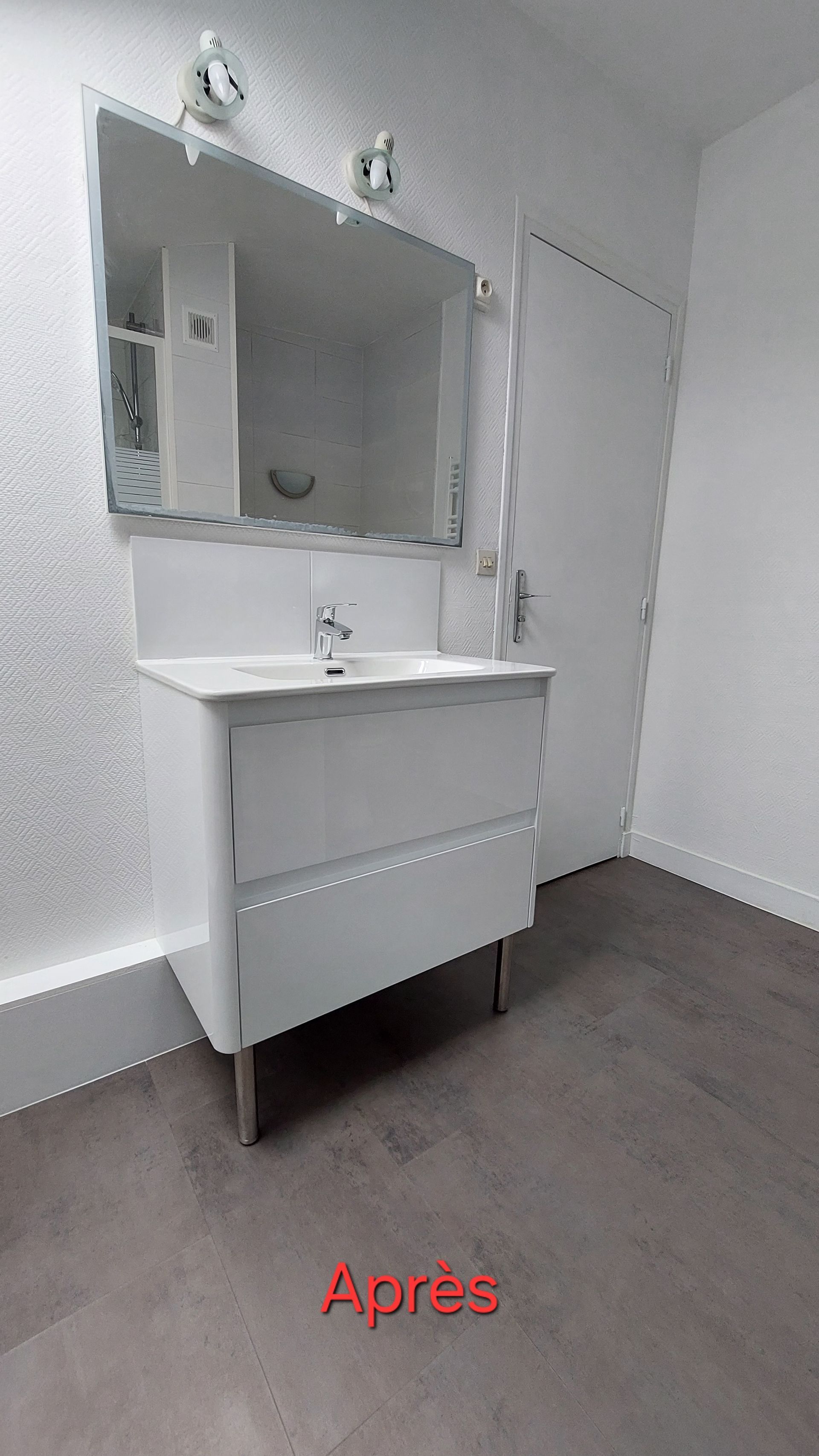 Salle de bains blanche avec lavabo, miroir et porte ; sol gris foncé ; mention Après en rouge.