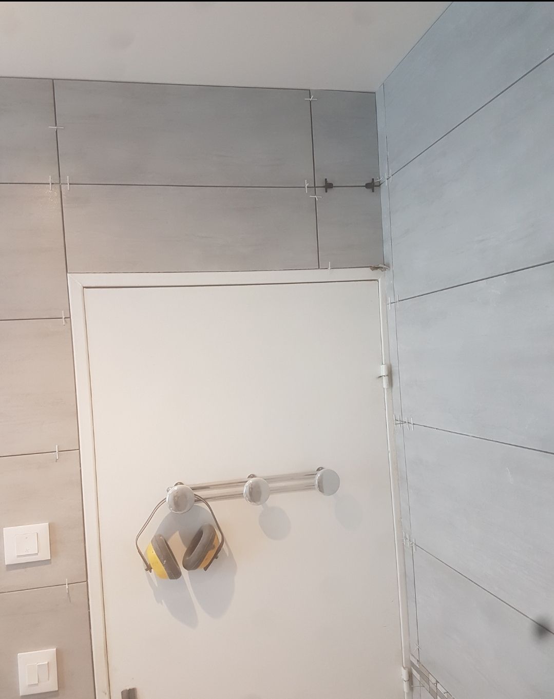 Intérieur de salle de bains avec murs carrelés gris clair, porte blanche et porte-serviettes.