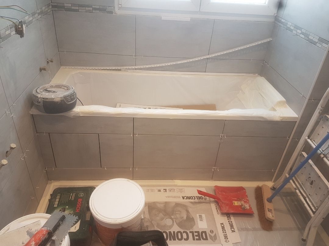 Rénovation de salle de bains en cours, avec une baignoire encastrée entourée de cloisons sèches, des outils et des matériaux éparpillés.