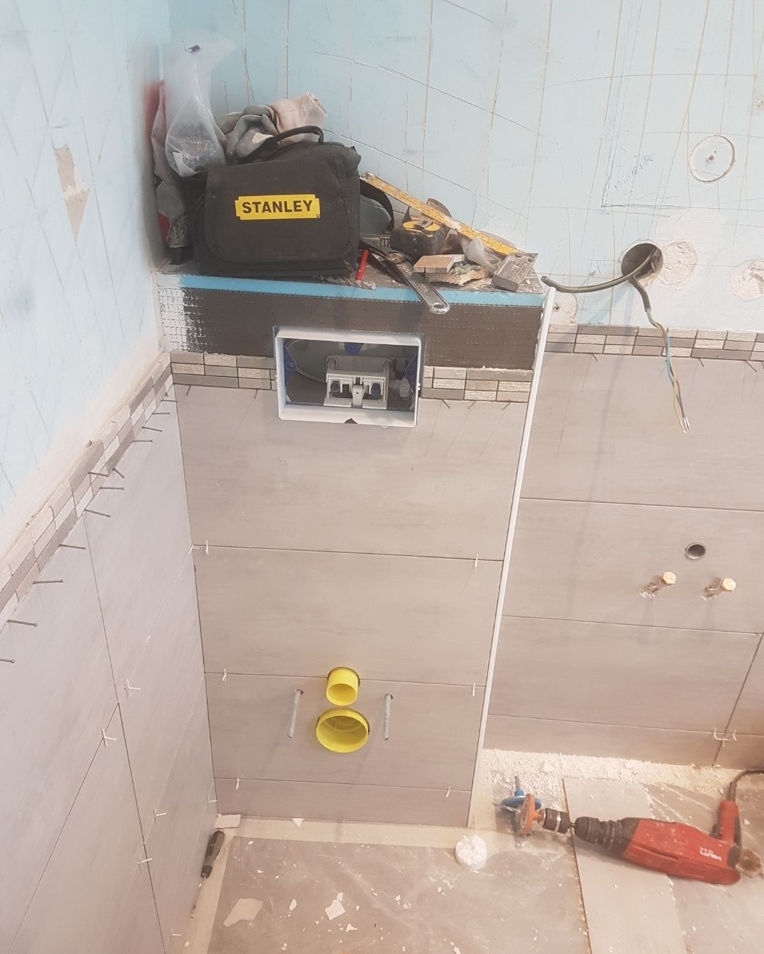 Salle de bains en rénovation avec panneaux muraux gris, arrivée d'eau pour les toilettes et outils.