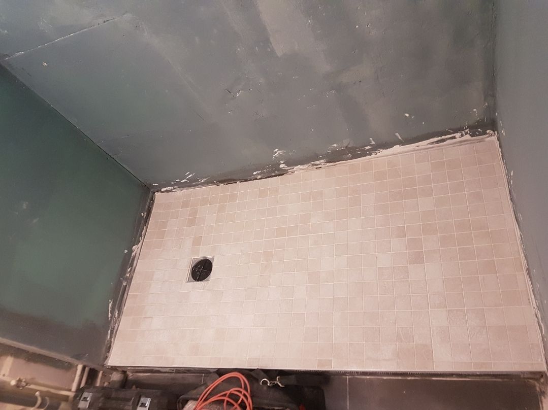 Cabine de douche en construction, avec sol carrelé, bonde foncée et murs bleu-gris.