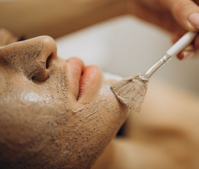 Persona que recibe un tratamiento facial con una mascarilla aplicada con un cepillo en un spa.