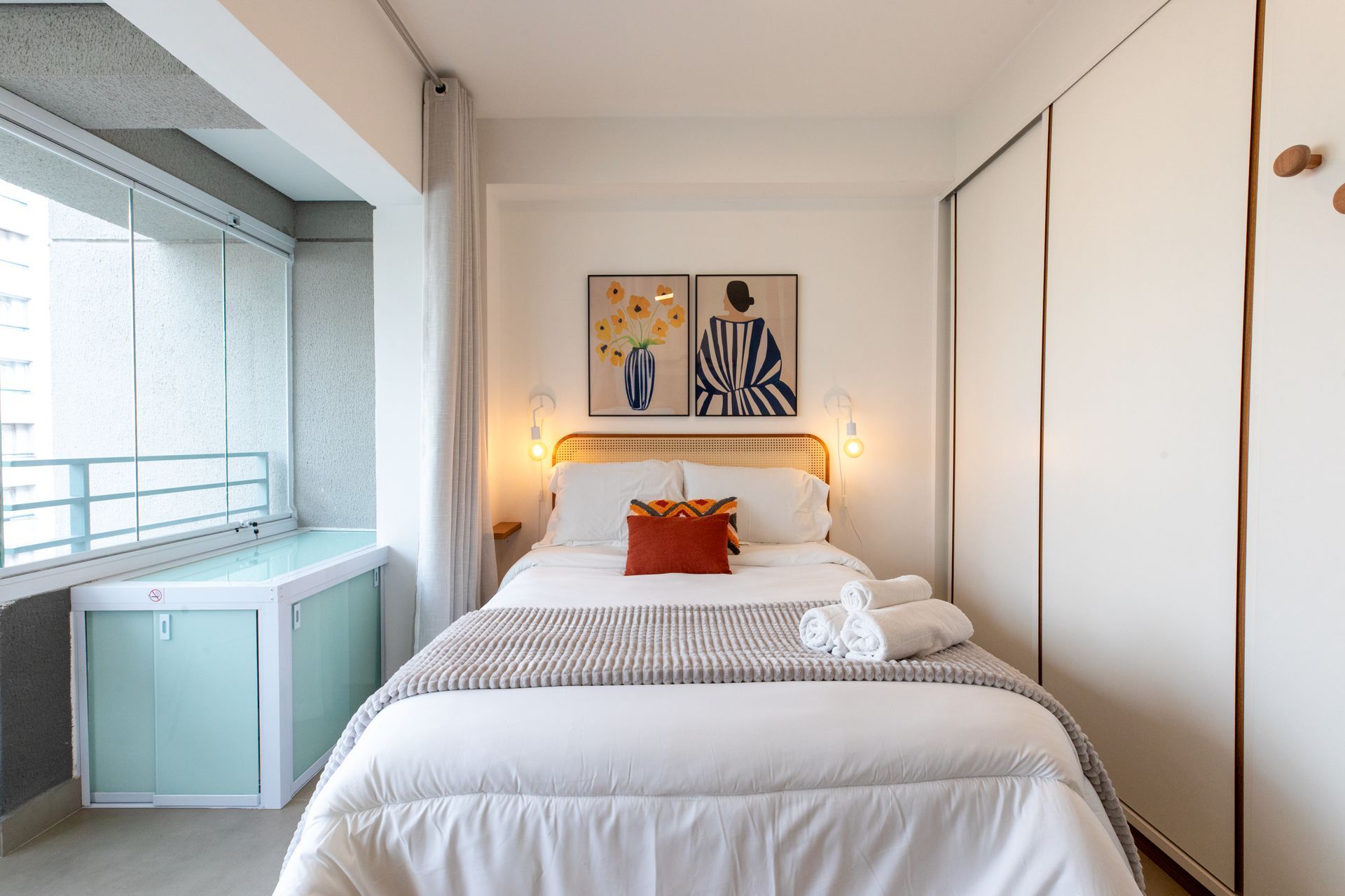 Bedroom with a bed, balcony, and closet. White and light-colored decor with two art prints.