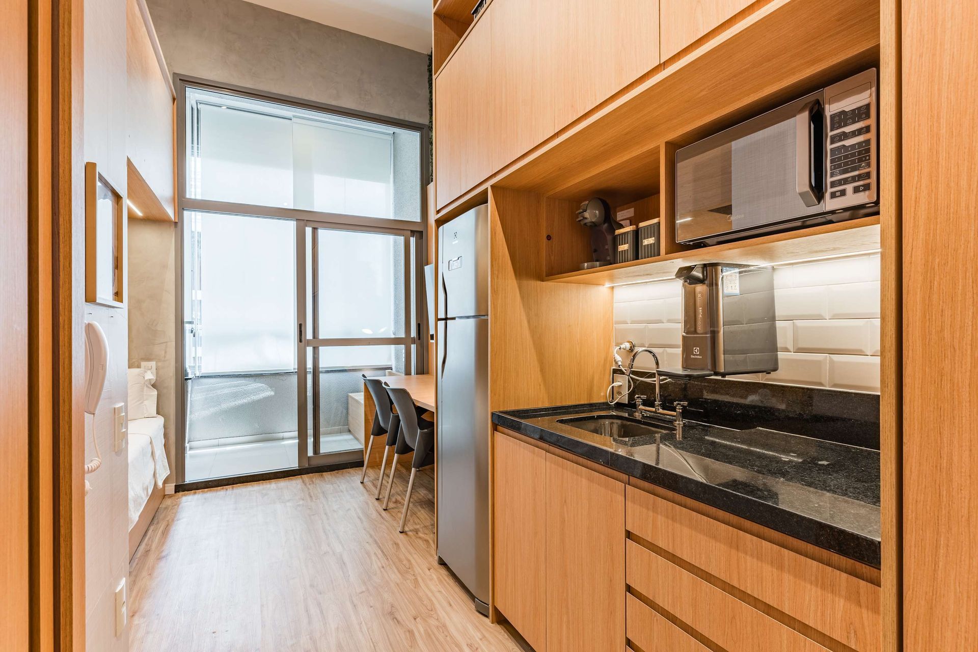 Small modern apartment kitchen with wooden cabinets, stainless steel appliances, and a window.