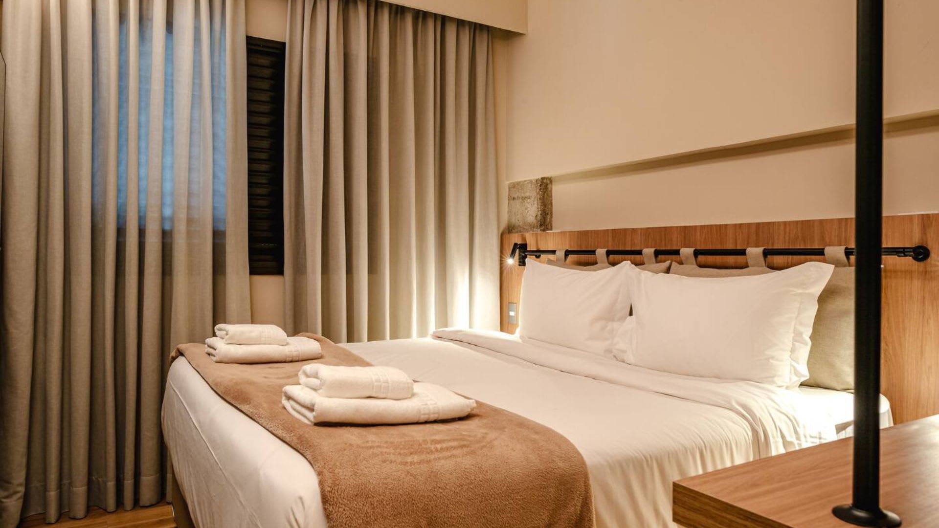 A hotel bedroom with a made bed, towels, and closed curtains.
