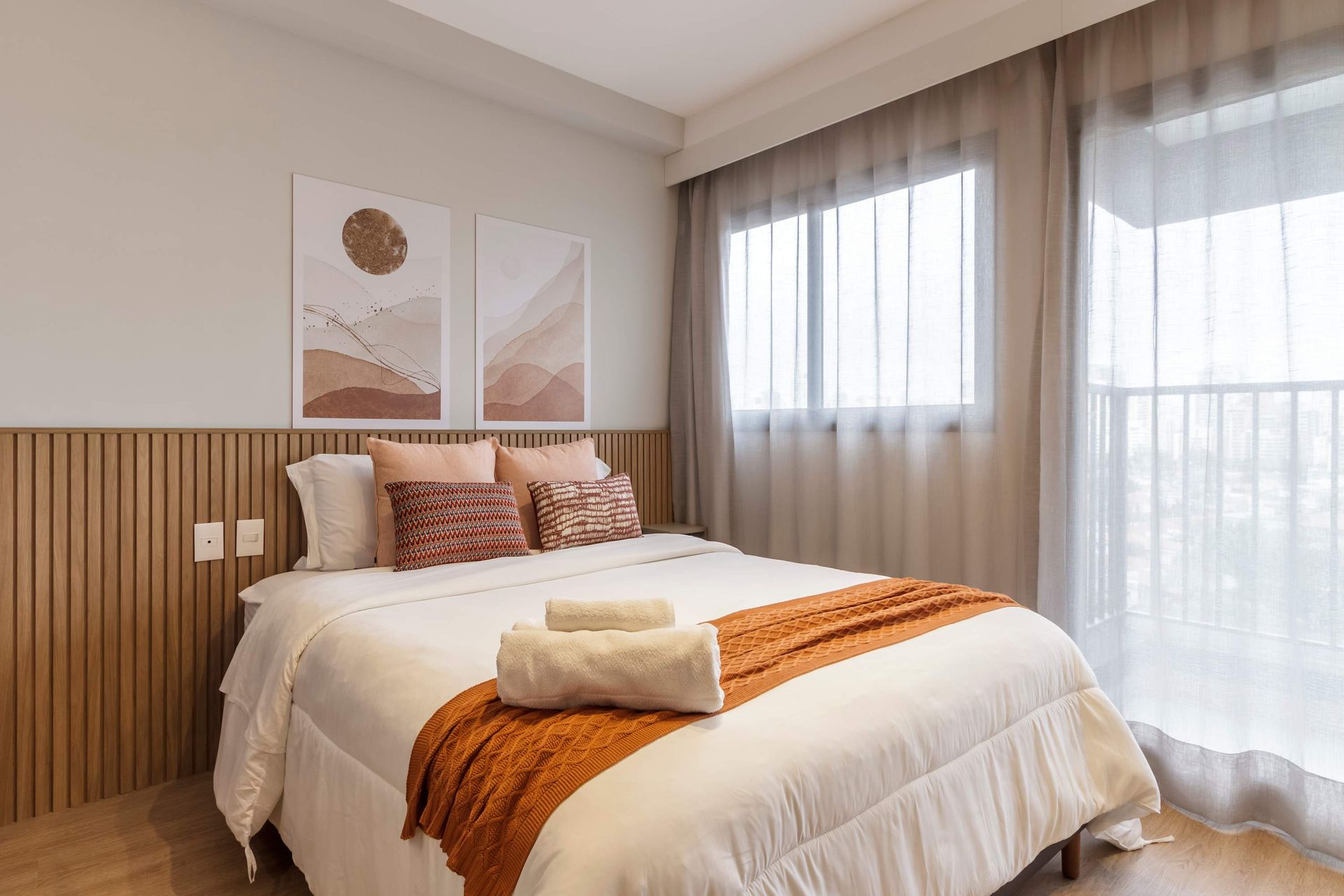 Bedroom with bed, art, and window with sheer curtains. Warm colors, wooden accents.