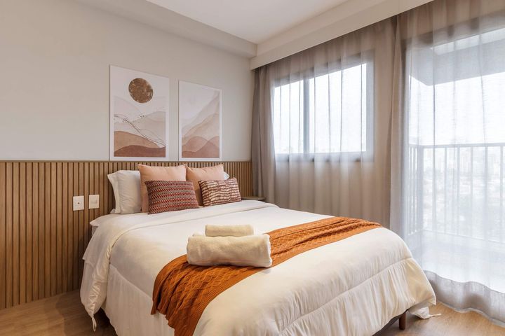 Bedroom with bed, art, and window with sheer curtains. Warm colors, wooden accents.