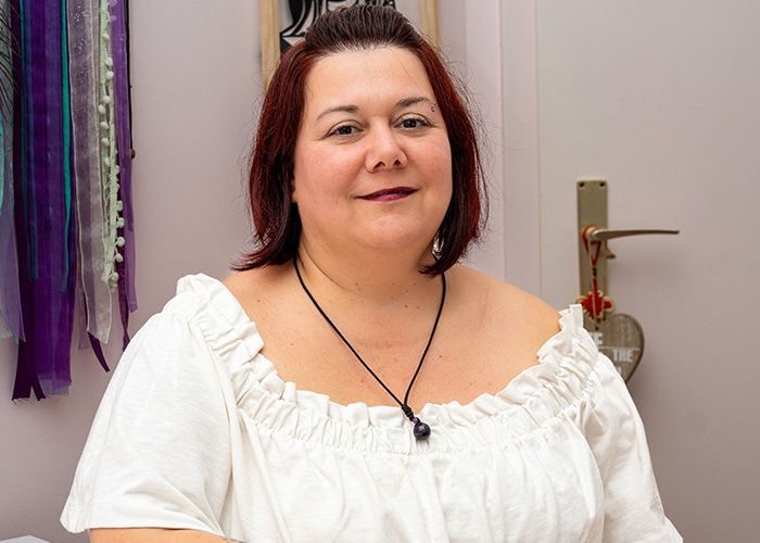 Femme souriante en blouse blanche à l’intérieur, à côté de rubans violets suspendus.