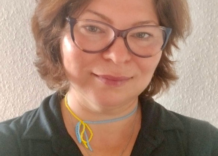 Portrait en gros plan d’une personne portant des lunettes, un haut noir et un collier coloré, qui sourit légèrement.