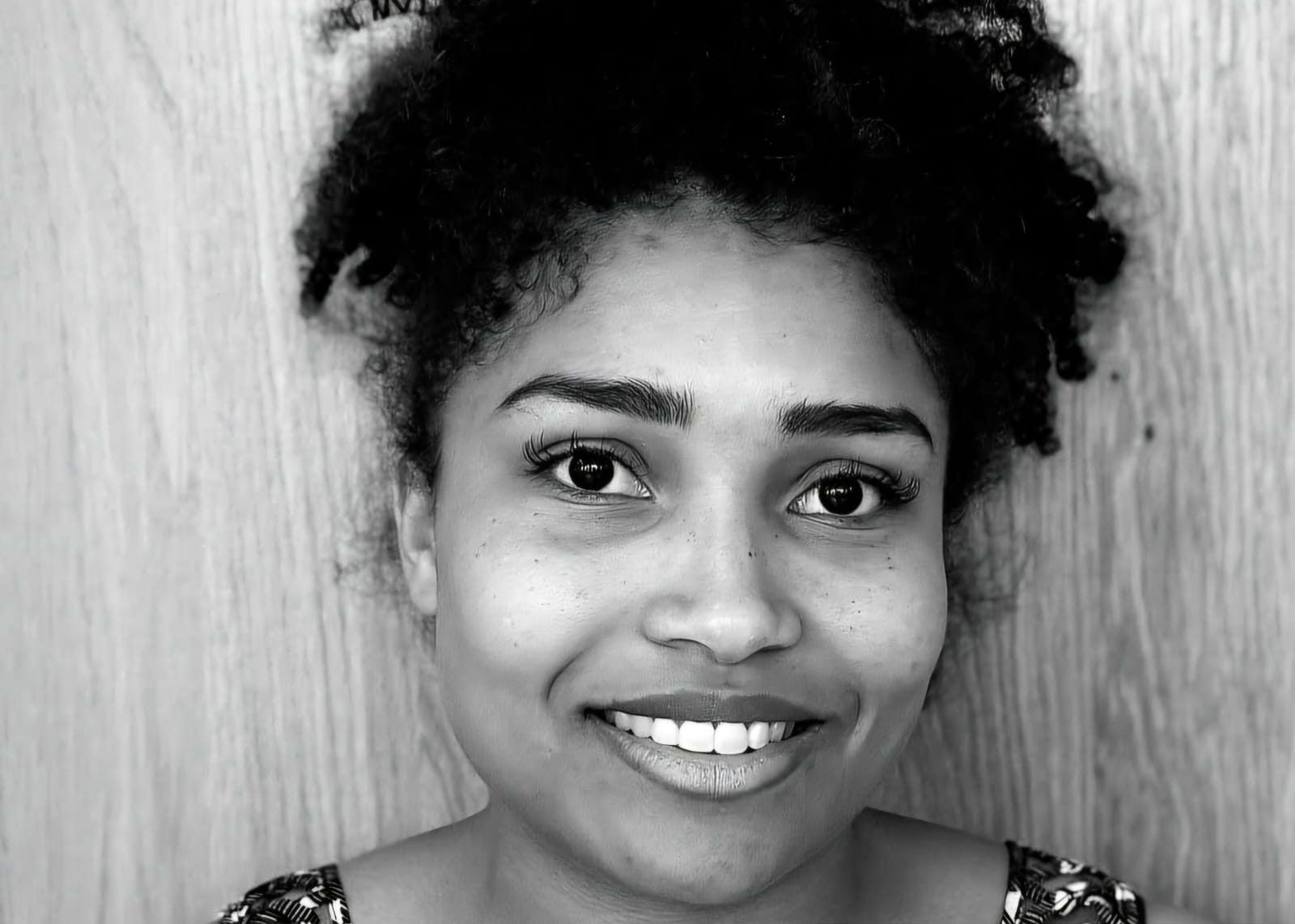 Personne souriante aux cheveux bouclés devant un fond en bois clair