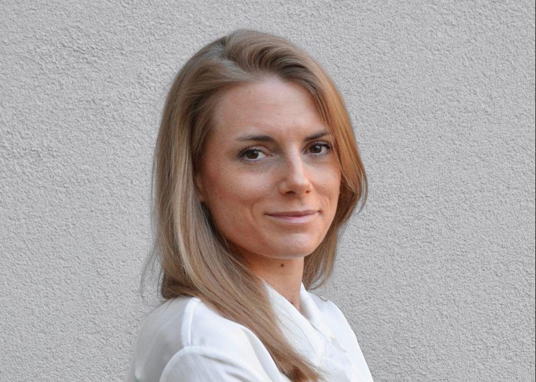 Portrait d’une femme blonde en chemisier blanc devant un mur gris clair