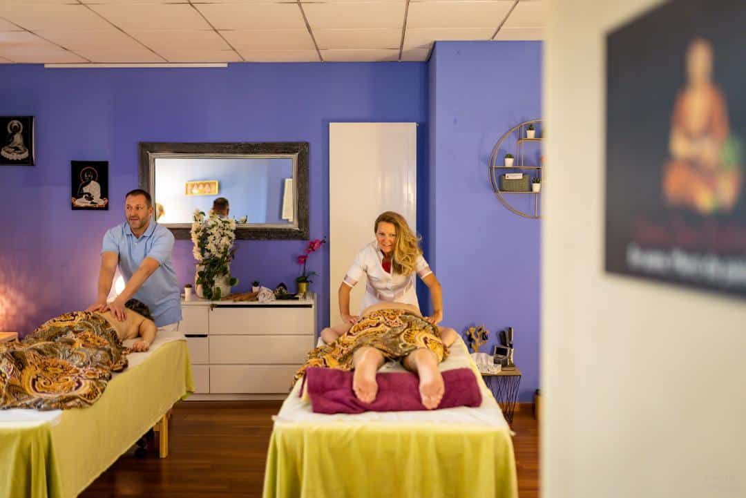Salle de massage avec deux tables de massage, des thérapeutes et des clients dans un spa aux murs bleus