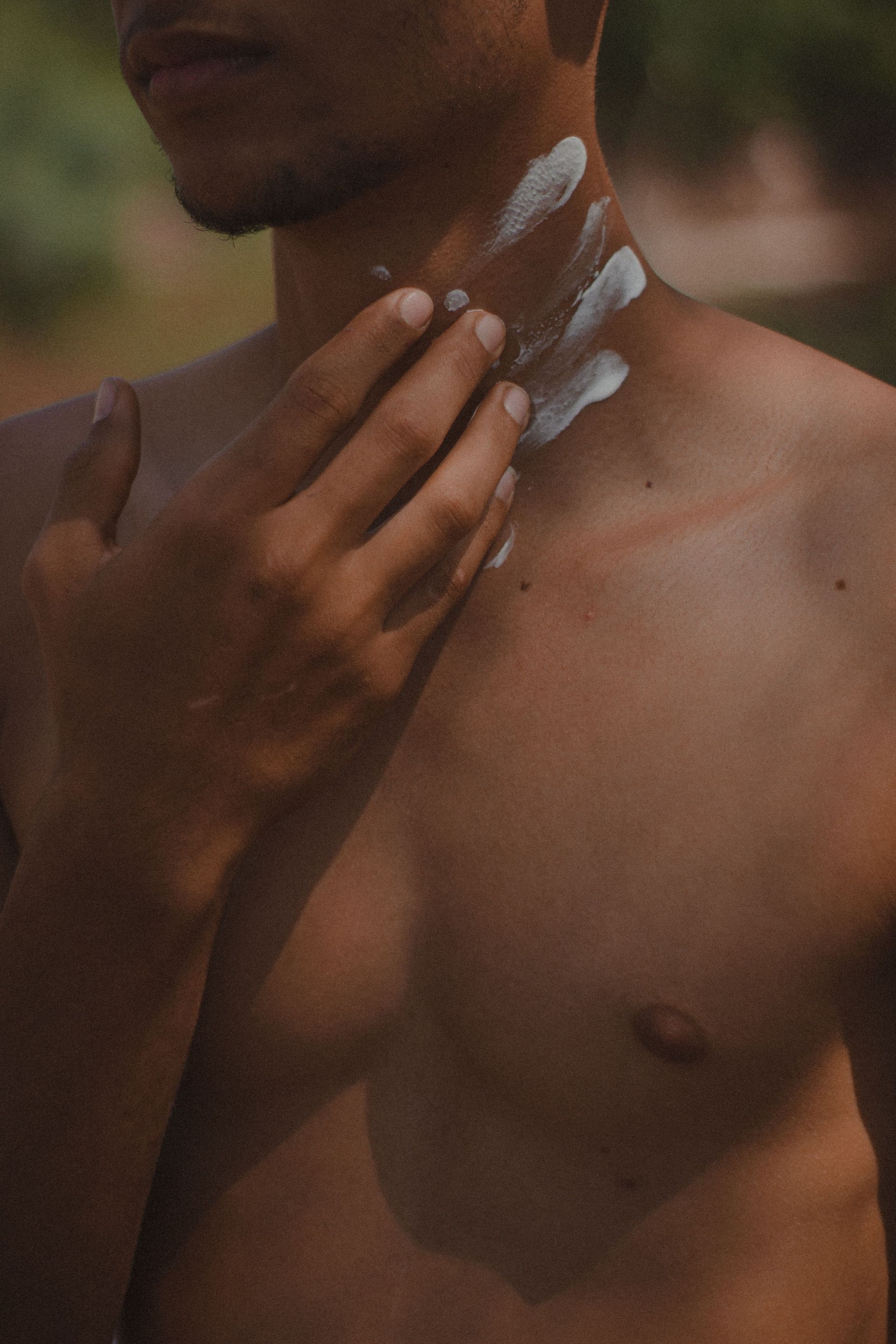 Personne appliquant de la lotion sur le cou et l’épaule, avec de la crème blanche visible sur la peau.