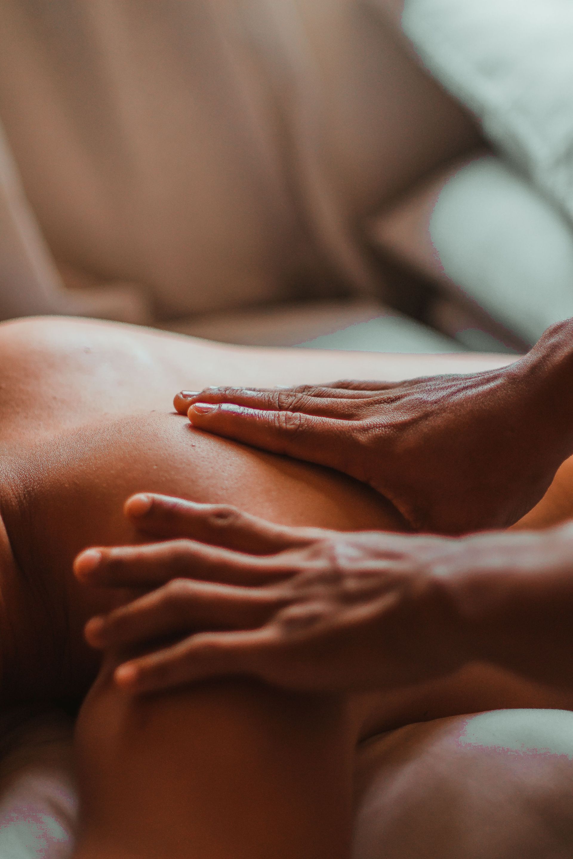 Des mains massent doucement le dos d’une personne dans un gros plan à la lumière douce et chaleureuse.