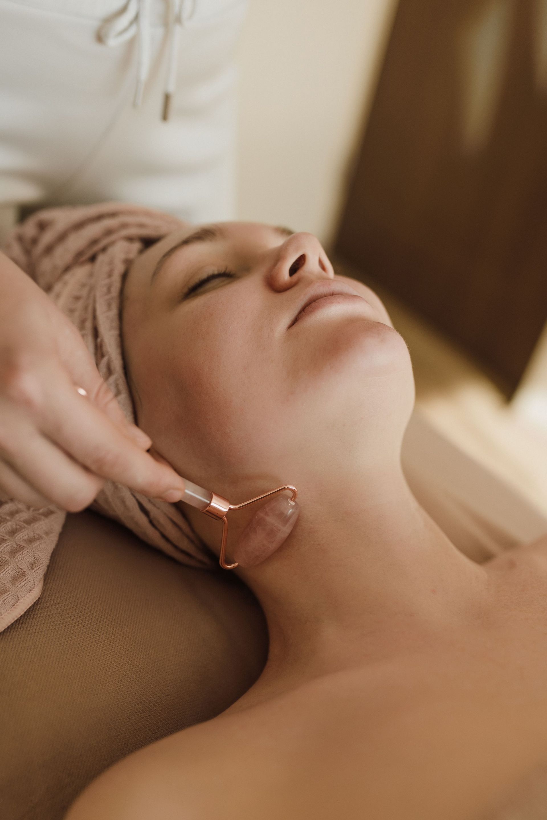 Massage du visage avec un outil en quartz rose sur une femme allongée sur une table de spa