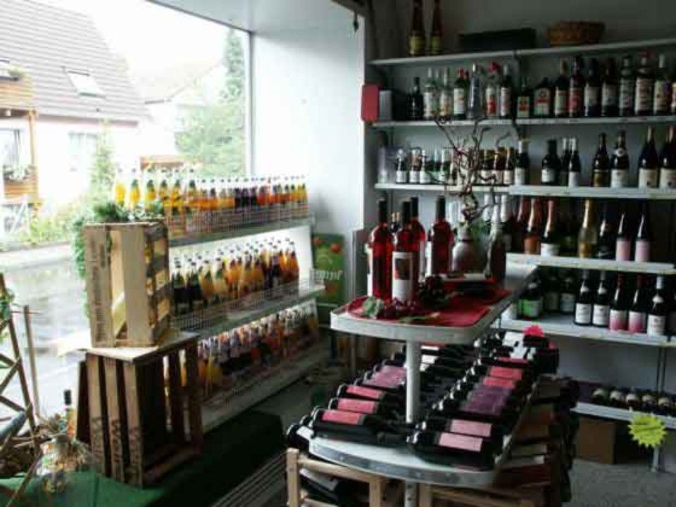 Blick in den Verkaufsraum mit einem Saftregal direkt vor dem Schaufenster und Weinregalen und Weinauslagen