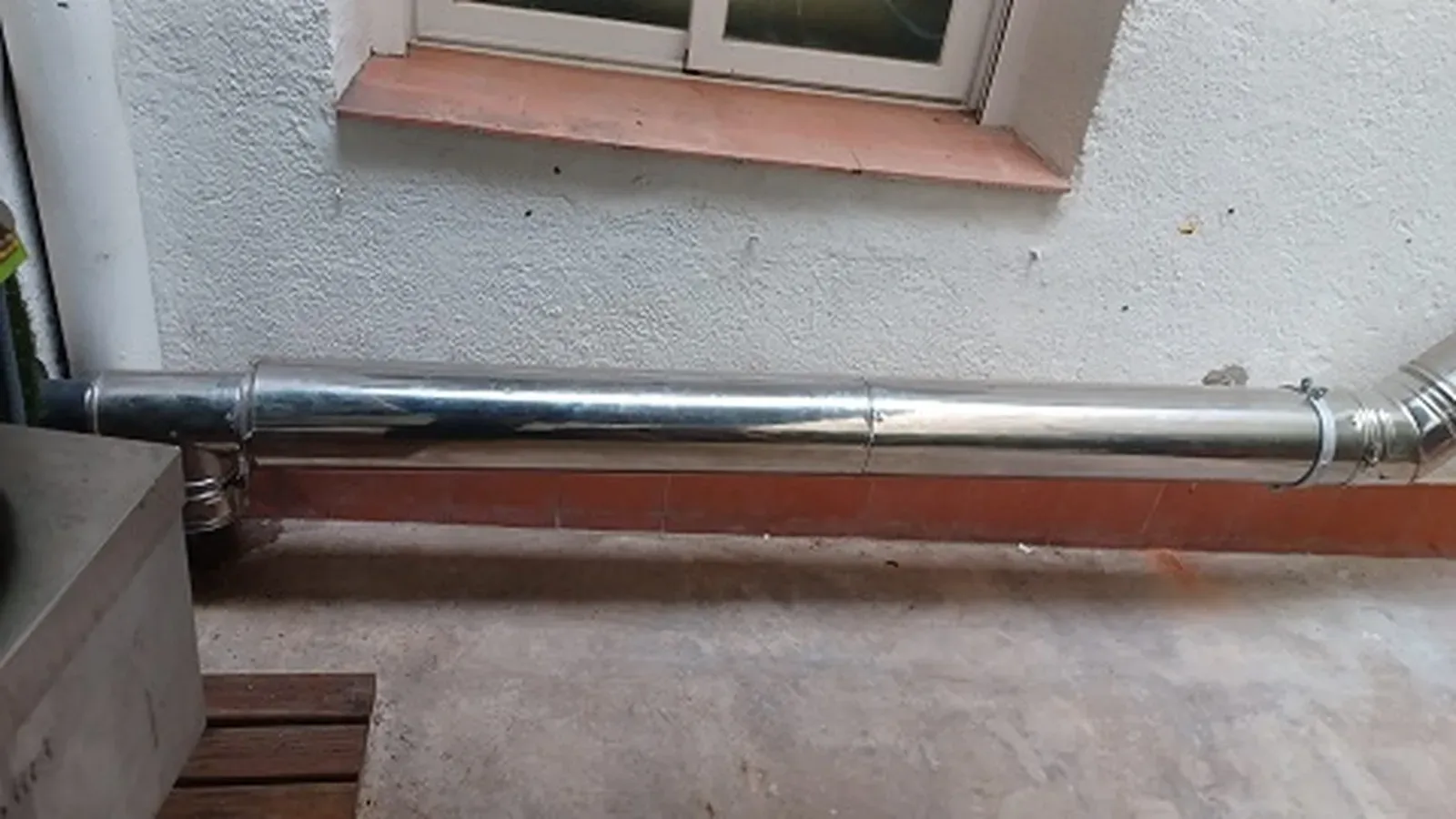 Tubo de escape de metal brillante fijado a la pared de un edificio.