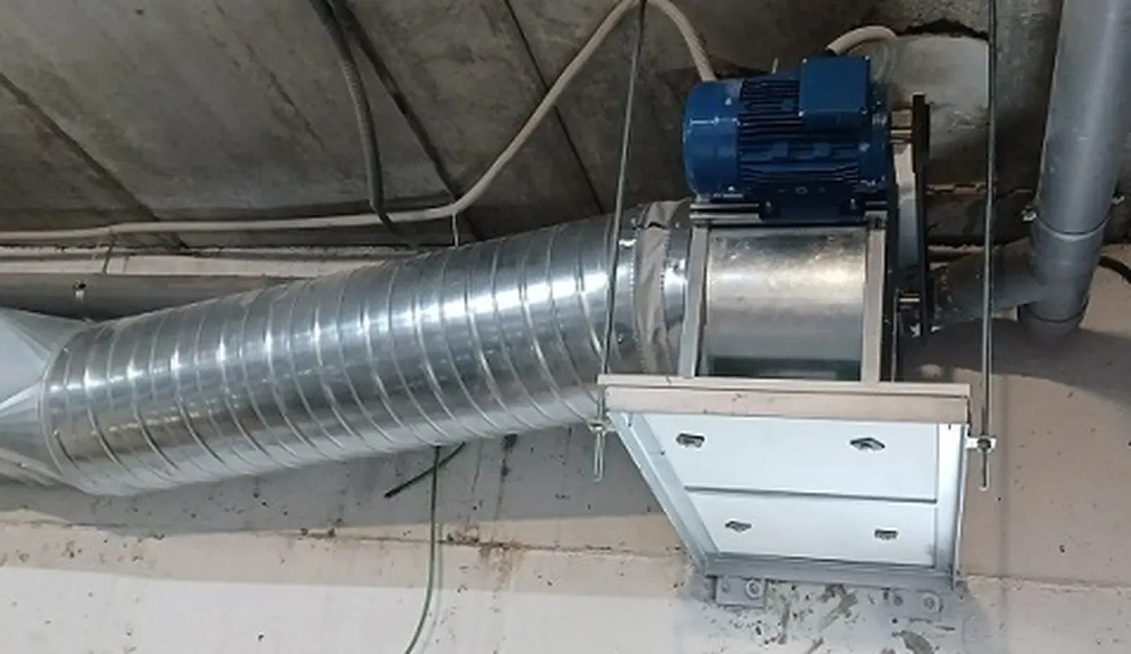 Sistema de ventilación metálico fijado a un techo con motor y conductos de color azul.