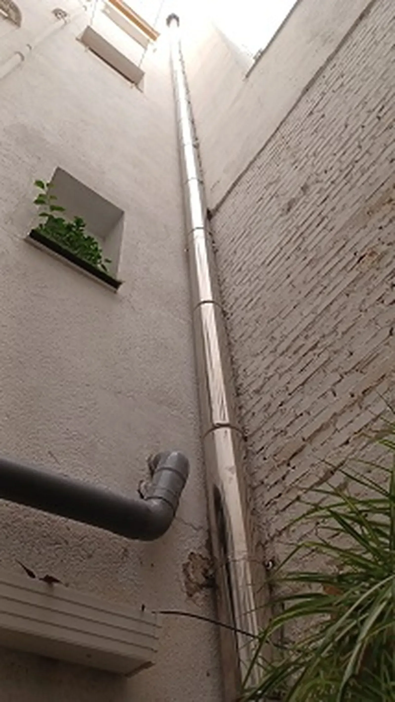 Una tubería de metal alta y brillante corre verticalmente entre dos edificios con una pequeña ventana