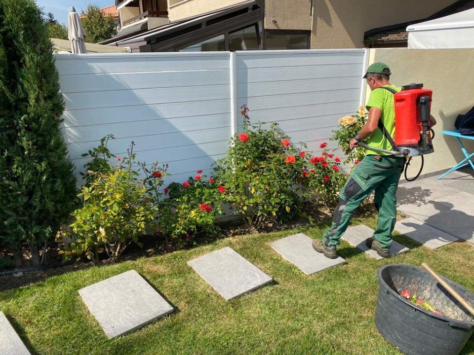 Un homme pulvérise des fleurs dans un jardin avec un sac à dos rouge.