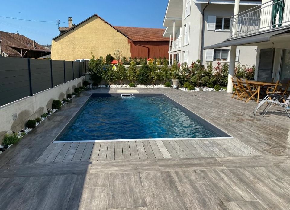 Une grande piscine avec une terrasse en bois devant une maison.