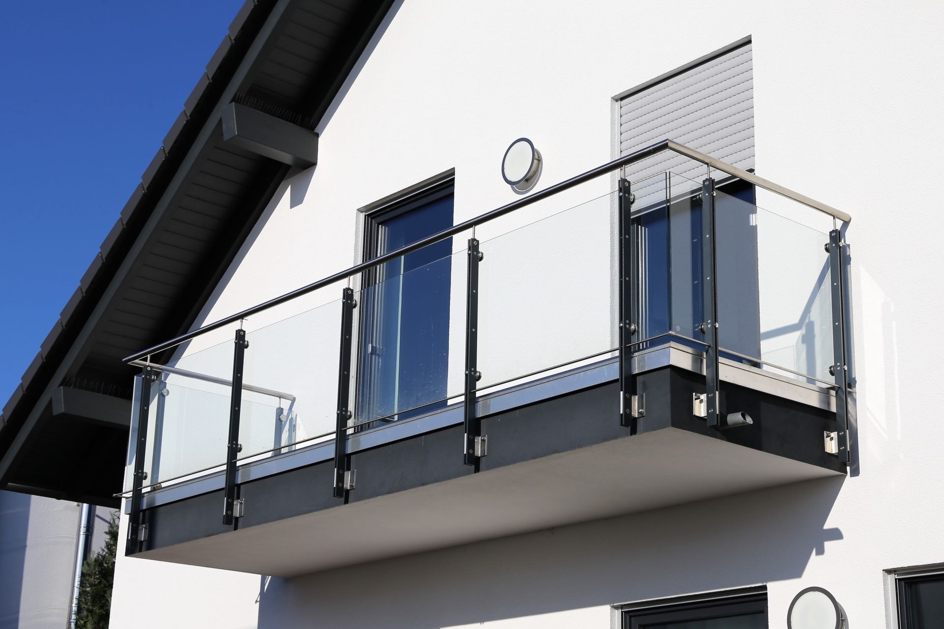 Modernes weißes Haus mit einem Balkon mit Glasgeländer und blauem Himmel darüber