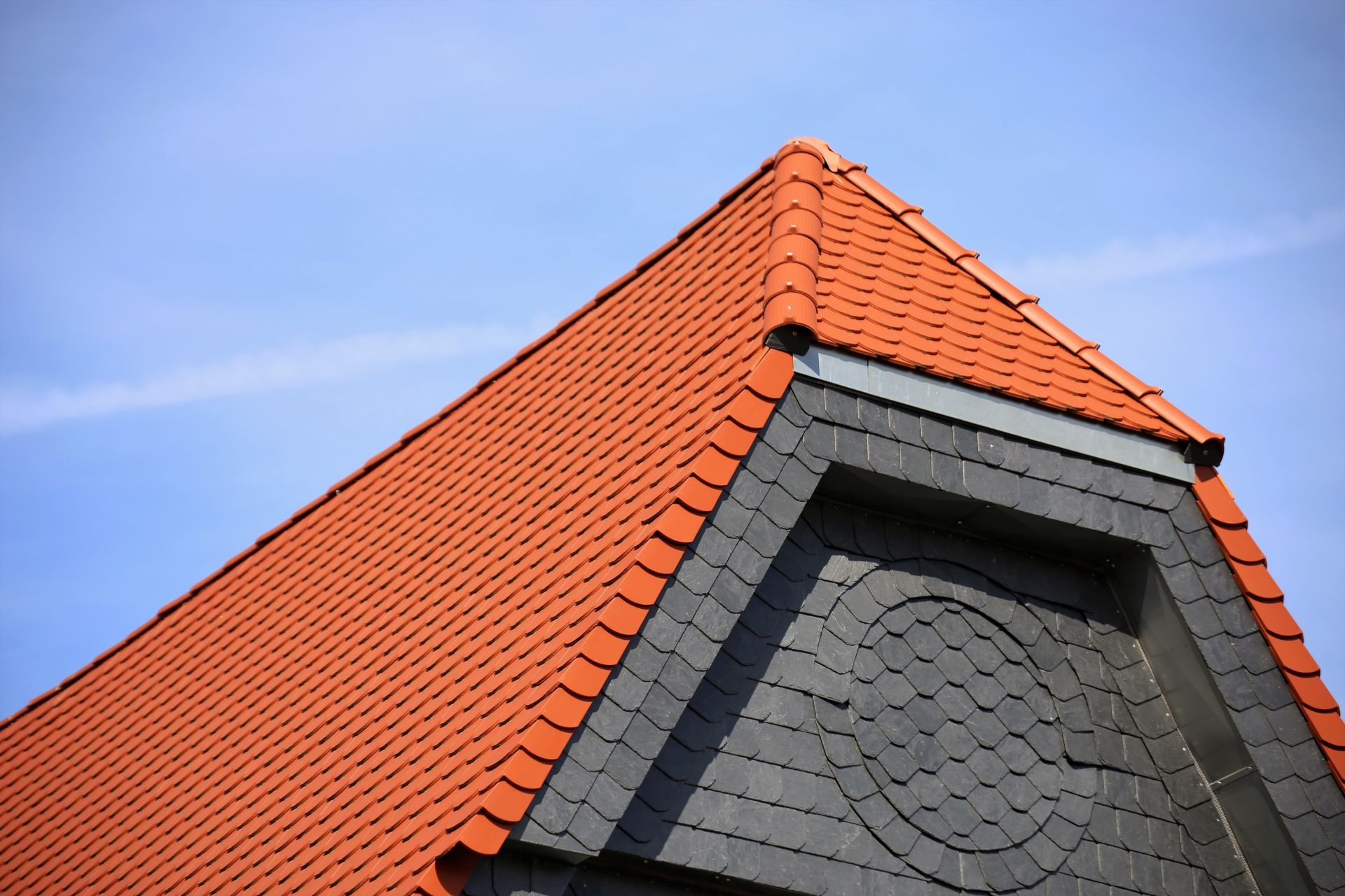 Rotes Ziegeldach mit grauer Dachgaube vor blauem Himmel