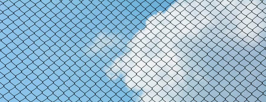 Un primer plano de una valla de alambre con un cielo azul de fondo.