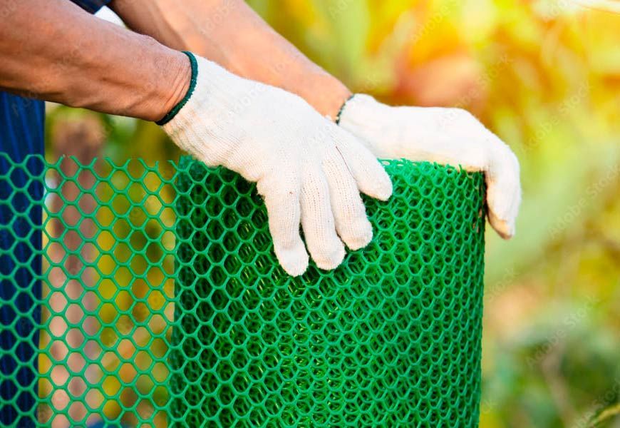 Una persona que lleva guantes blancos sostiene un rollo de malla de plástico verde.