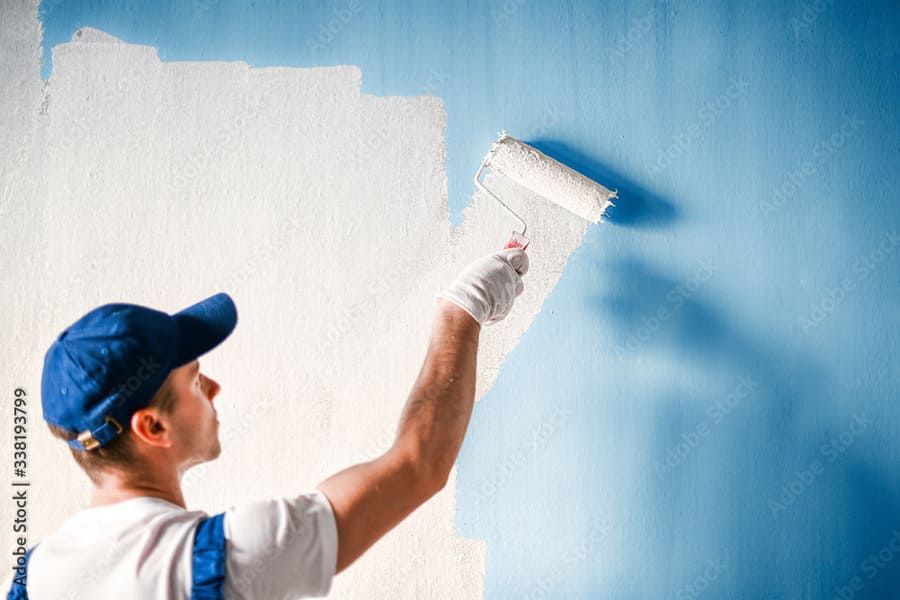Un hombre está pintando una pared azul con un rodillo de pintura.