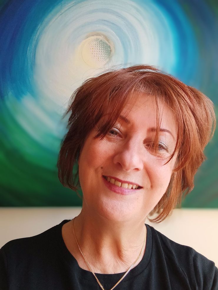Femme aux cheveux châtain roux souriante, vêtue d'un haut noir, avec une peinture abstraite bleue et verte en arrière-plan.