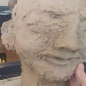 Sculpture en argile représentant une tête et un visage humains grossiers tenus par une main
