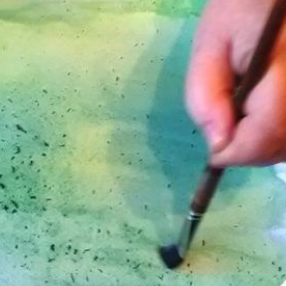 Main tenant un pinceau, appliquant de la peinture foncée sur une toile verte